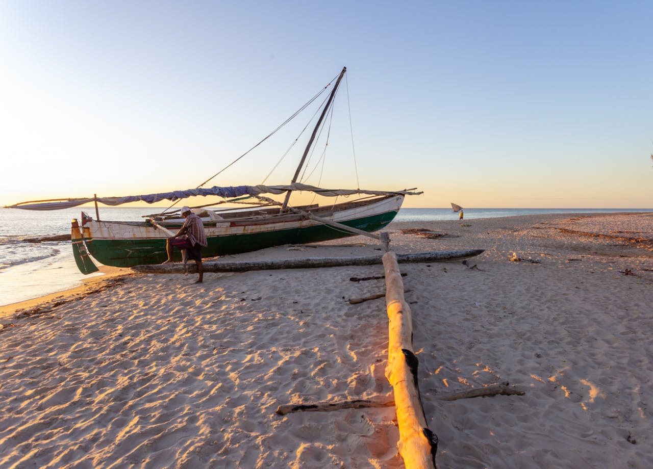 about-02 A serene beach scene in Madagascar with a traditional fishing boat during sunset on the sandy shore.